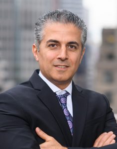 Alex Omrani posing in a black suit and blue tie