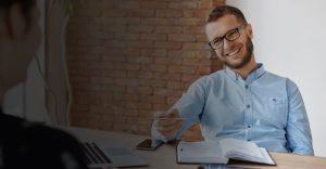 young male sitting at desk with open book smiling