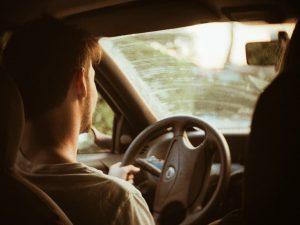 male driver behind the wheel of a car with a dirty windshield