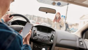 woman on phone driving with pedestrian in front of the car