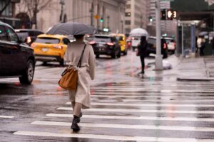 Mujer con paraguas cruzando calle en Manhattan, explicando los beneficios de No-Fault para peatones en Nueva York.