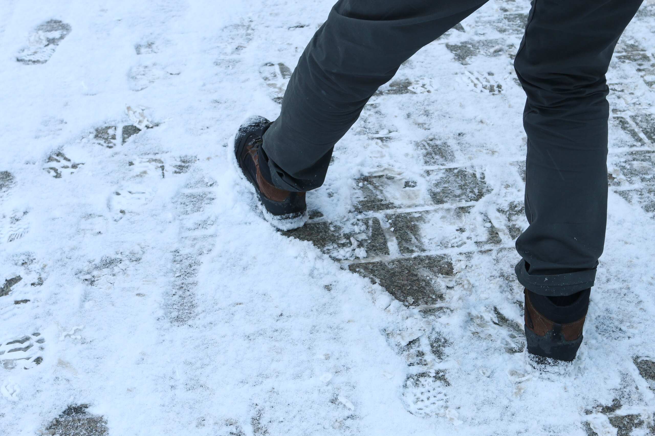 Peatón caminando sobre una acera nevada mientras sigue cayendo nieve, ejemplo de cuándo puede aplicarse la defensa de tormenta en curso en Nueva York.