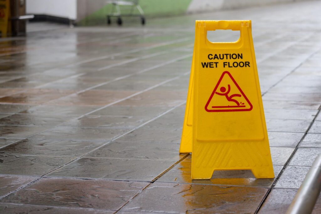 Yellow caution wet floor sign on a slippery tile walkway, representing a common cause for a New York slip and fall accident lawyer to file a claim.