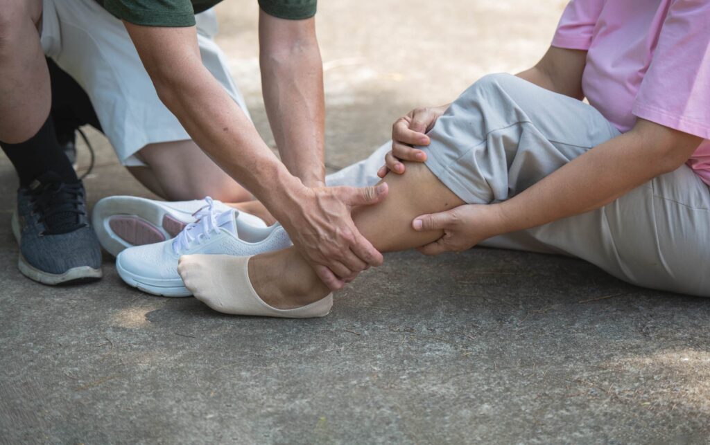 A person holding their injured ankle after a fall on pavement, highlighting the need for a New York slip and fall accident lawyer to recover medical damages.