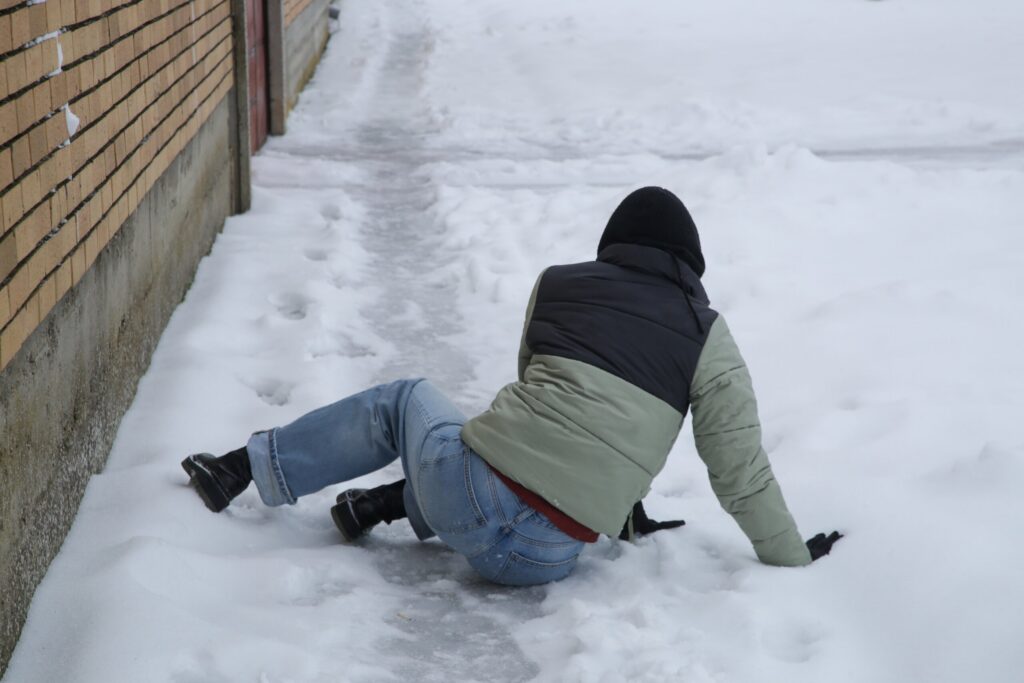 Person slipping on an icy sidewalk in New York, illustrating landlord liability under NYC Administrative Code §7-210.
