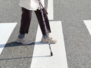 An injured person using a cane to walk across a city street, a case commonly handled by a New York pedestrian accident lawyer.