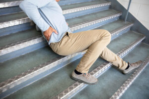 Hombre con dolor de espalda tras caerse en escaleras metálicas, imagen para servicios de un abogado de accidentes por resbalones y caídas en Nueva York.