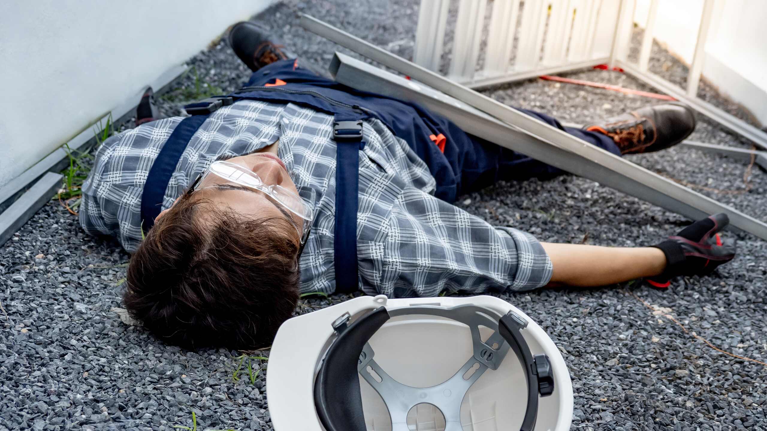 An injured worker lying on the ground next to a fallen ladder on a New York construction site after a failure of gravity-related safety equipment.