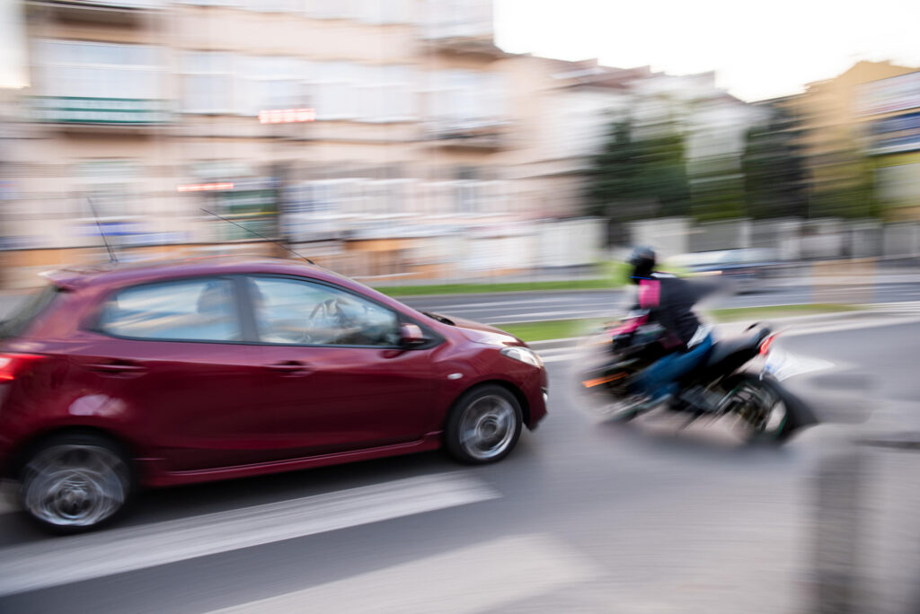 A red car colliding with a motorcycle in a busy New York intersection, representing the common risk of vehicle collisions for motorcyclists.