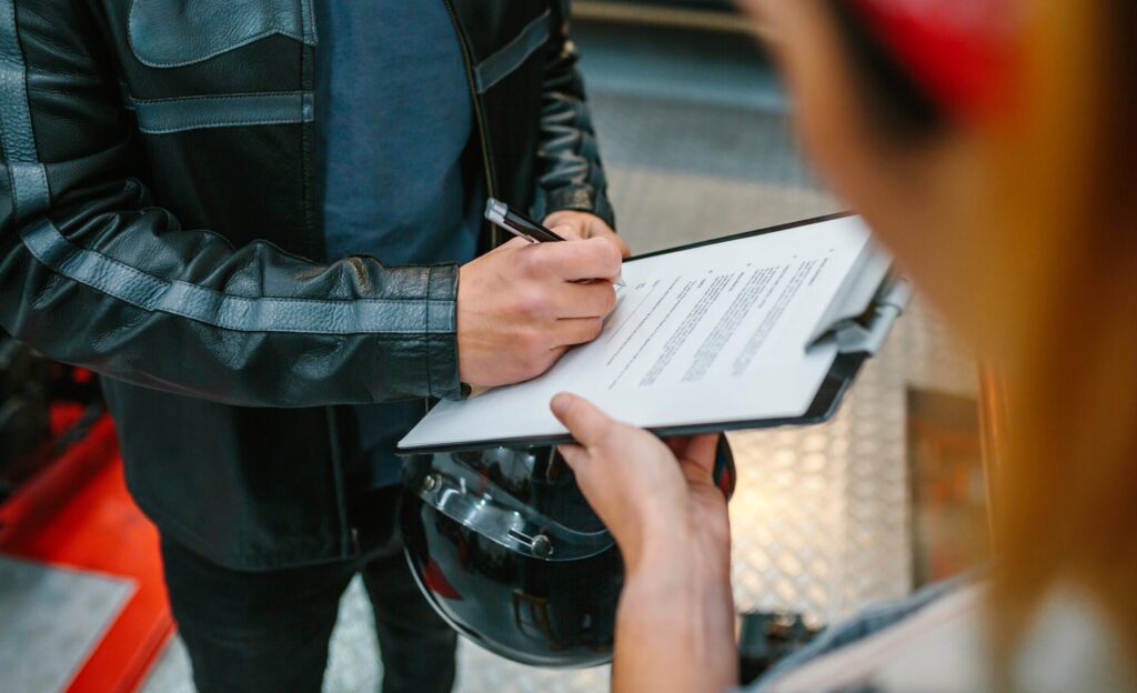Motorcyclist in a leather jacket signing legal documents and insurance paperwork in New York.