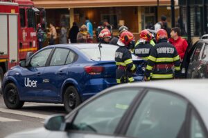 Emergency responders in "Pompierii" gear stand next to a blue Uber vehicle with rear-end damage at an accident scene.