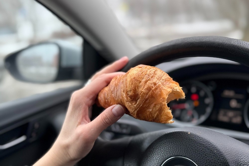 Driver eating while holding the steering wheel, a form of distracted driving that causes New York car accidents