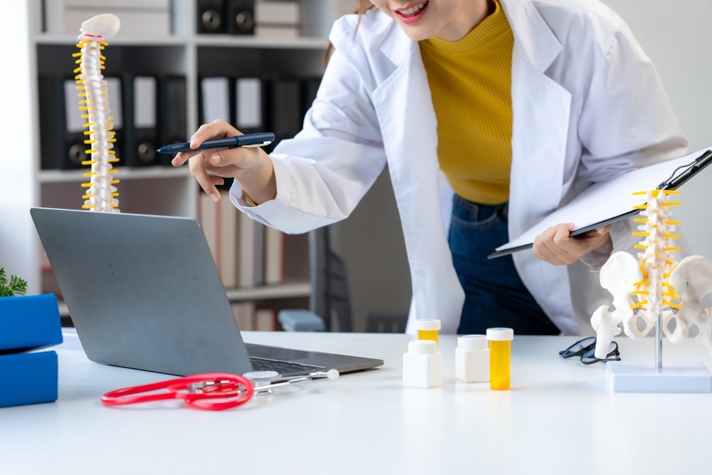 Doctor reviewing spinal cord imaging on a laptop with a spine model on the desk