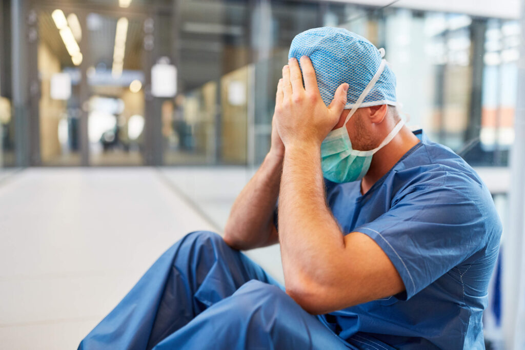 A stressed surgeon sitting on the floor with head in hands following surgical errors in NYC hospitals.